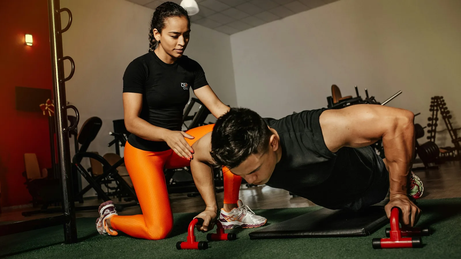 Coach agenouillée qui corrige la posture d'un pratiquant pendant des pompes