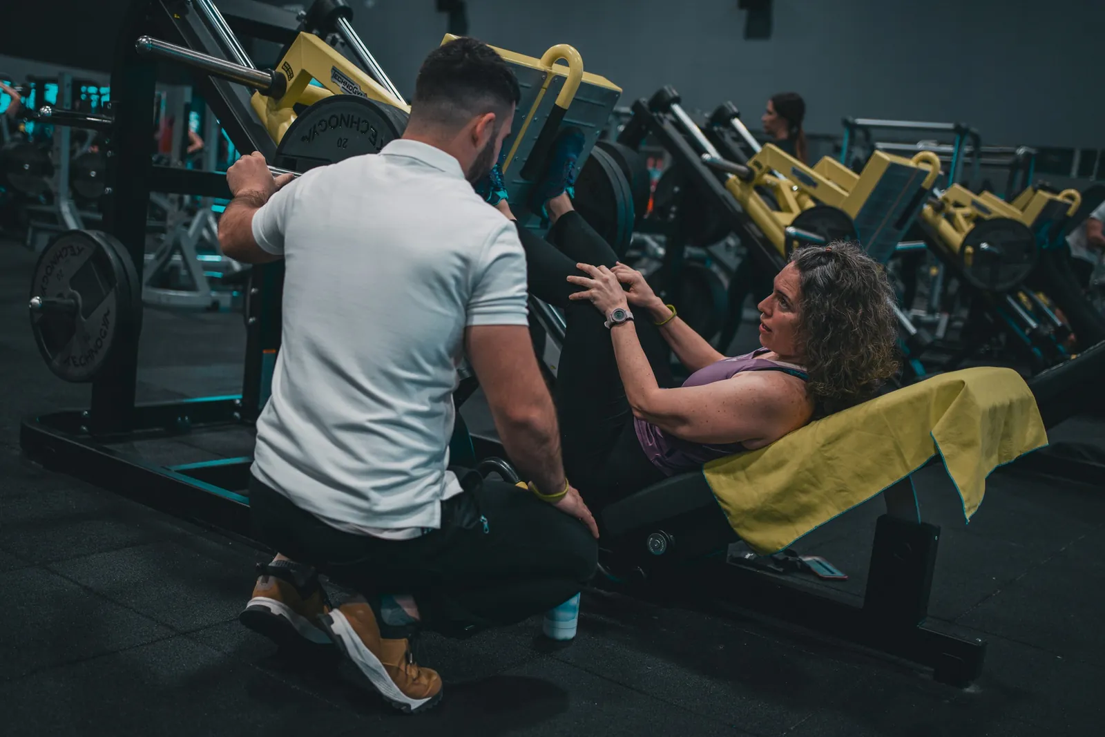 Coach accompagnant une pratiquante sur une presse à cuisses en salle de musculation